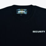 Close-up of a black crewneck t-shirt with SECURITY printed in white on the chest and an addos brand label inside the collar.