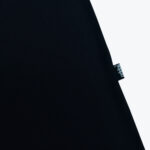 Close-up of a black fabric garment showing a small black side tag with the white Addos logo.