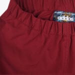 Close-up of the elastic waistband of burgundy Addos workwear pants, showing the gathered fabric and a colorful inner label with the Addos logo.