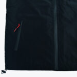 Close-up of a black technical jacket showing a taped main zipper, a side pocket with a red zipper pull, and a bottom hem drawstring toggle.