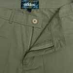 Close-up of the front zipper, button, and waistband of khaki ripstop workwear pants with an Addos Collection label.