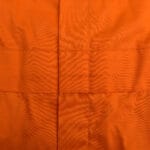 Close-up of bright orange fabric featuring vertical and horizontal stitched seams forming a grid pattern.