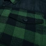 Close-up of a green and black plaid flannel shirt jacket featuring a chest pocket with a black snap button and a black fabric yoke.