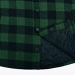 Close-up of a green and black plaid flannel shirt jacket showing black snap buttons and a black quilted inner lining.