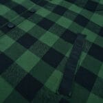 Close-up of a green and black buffalo plaid shirt showing snap buttons and a vertical welt pocket.