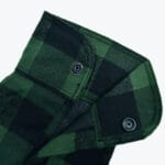 A close-up shot of a green and black plaid garment featuring metal snap buttons.