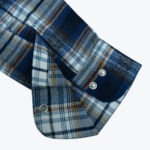 Close-up of a blue, white, and brown plaid flannel shirt cuff with silver snap closures.