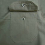 Close-up of a khaki fabric pocket with its flap flipped up, revealing a silver snap button fastener.