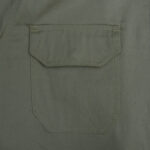 Close-up of an olive green fabric pocket with a flap and double stitching.