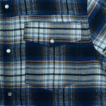 Close-up of a blue, white, and brown plaid flannel shirt showing a chest pocket with a pearl snap button.