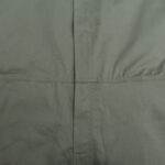 Close-up of a sage green garment showing a vertical placket meeting a horizontal waist seam with neat stitching.