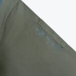 Close-up of an olive green garment sleeve showing five printed safety pictograms indicating protective standards like flame and electrical resistance.