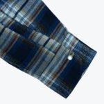 Close-up of a blue, white, and brown plaid flannel shirt cuff with a single white pearl snap button on a white background.