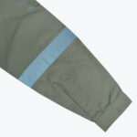 Close-up of an olive green work shirt sleeve featuring a wide light blue reflective safety band and printed safety icons near the shoulder.