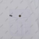A close-up of a white shirt pocket with a pointed flap, a central button, and a small black tag on the side.