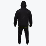 Back view of a person wearing a black hoodie with the hood up and matching black sweatpants, featuring a thin neon green line at the bottom hem of the hoodie.