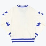 The back view of an off-white knit sweater with royal blue striped trim on the collar, cuffs, and hem, and blue graphic details on the sleeves.