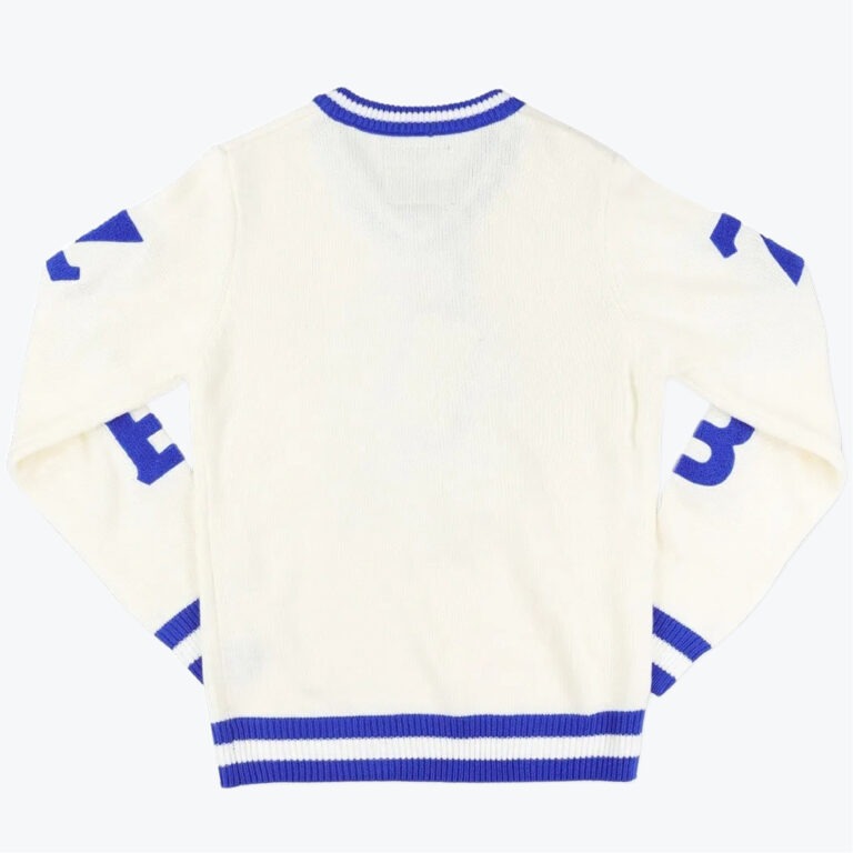 The back view of an off-white knit sweater with royal blue striped trim on the collar, cuffs, and hem, and blue graphic details on the sleeves.