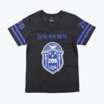 A black v-neck jersey shirt with ZETA PHI BETA printed in blue above the sorority's blue and white crest. The sleeves have blue stripes and Greek letters.