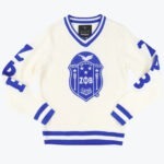 An off-white knit V-neck sweater with royal blue striped trim, featuring a large Zeta Phi Beta sorority shield emblem in the center and blue lettering on the sleeves.