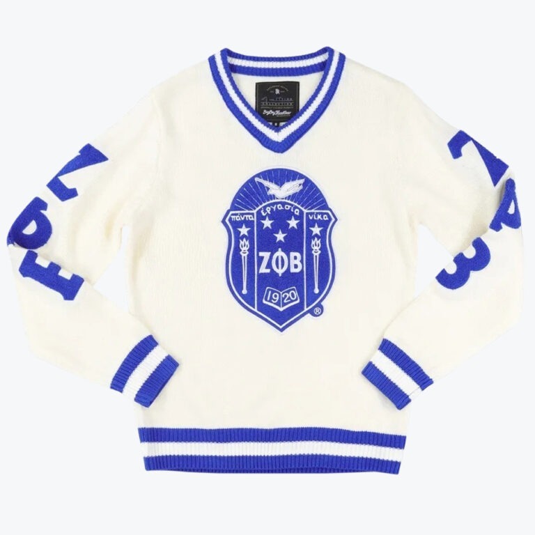 An off-white knit V-neck sweater with royal blue striped trim, featuring a large Zeta Phi Beta sorority shield emblem in the center and blue lettering on the sleeves.