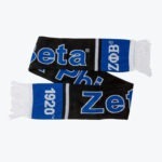 A black and blue knitted scarf with Zeta Phi Beta written on it, featuring the Greek letters ΖΦΒ and the year 1920 on blue end panels with white fringe.