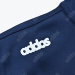 Close-up of a dark blue fabric garment with a white embroidered logo spelling "addas" instead of "adidas", surrounded by a faint repeating pattern of the same misspelled word.