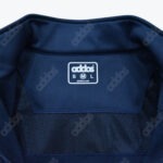 Close-up of the inner collar of a navy blue jacket showing a white label with addos and size M circled, set against a background of fabric with a mesh lining.